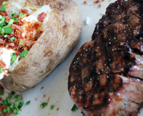 close up view of baked potato with all the fixings and steak