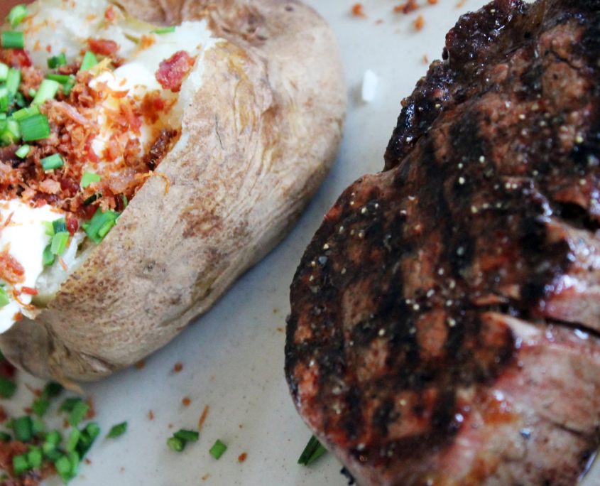 close up view of baked potato with all the fixings and steak